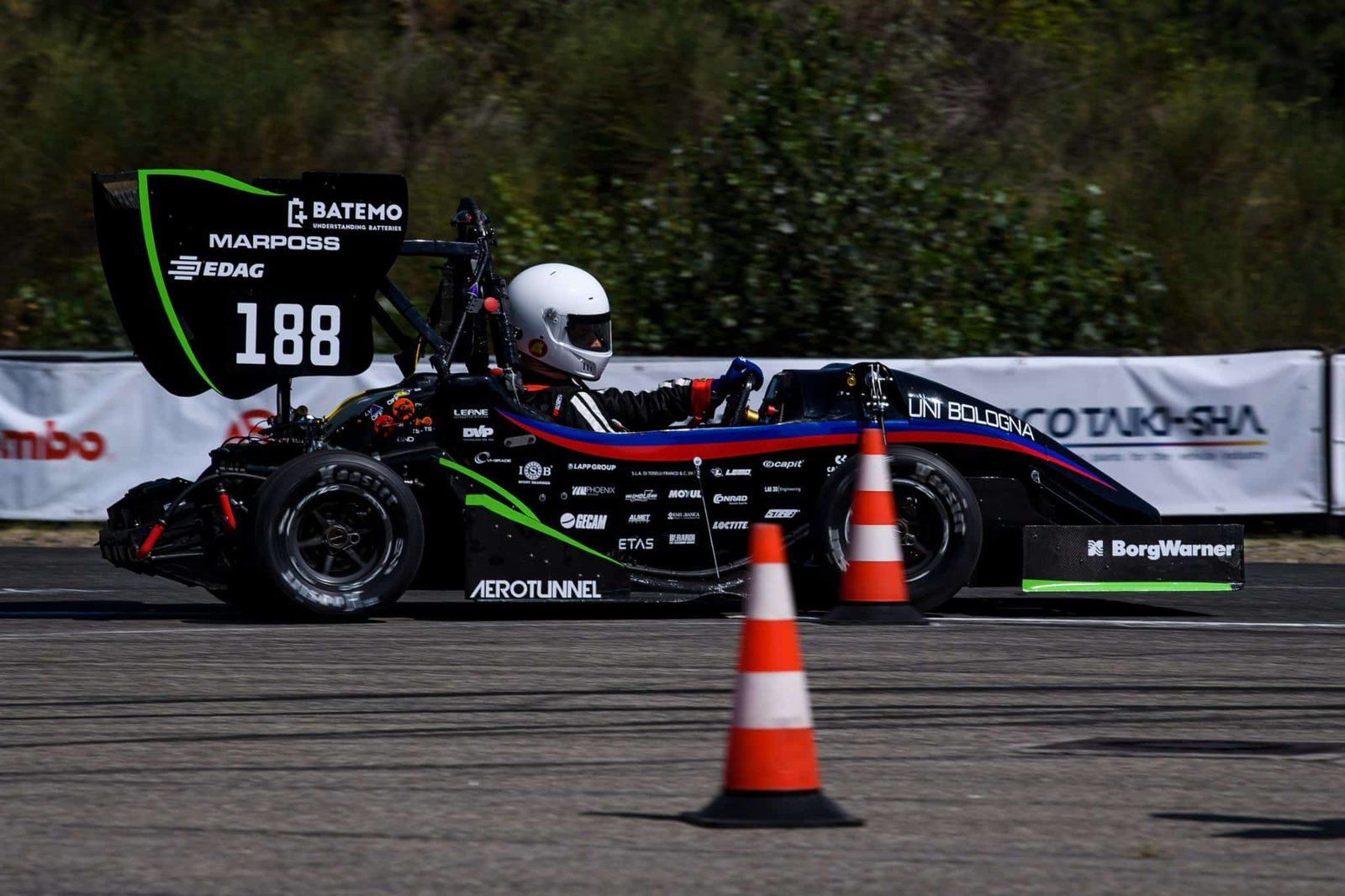 테스트 트랙에서 교통 콘 사이를 지나는 Formula Student 레이스카의 후방 윙에 Batemo 로고가 표시되어 있습니다.