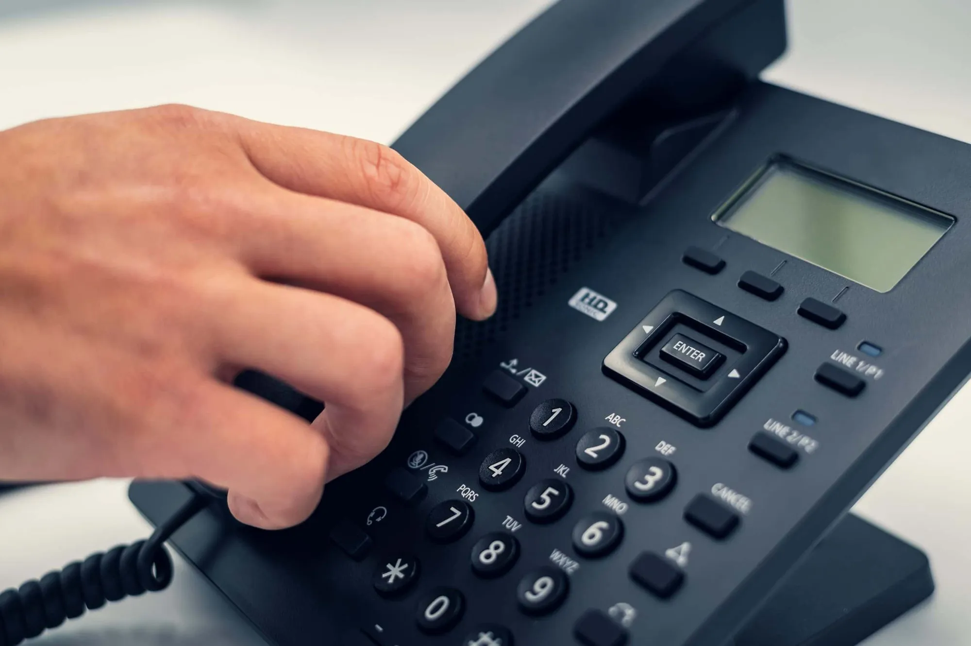 A hand dialing on a desk telephone